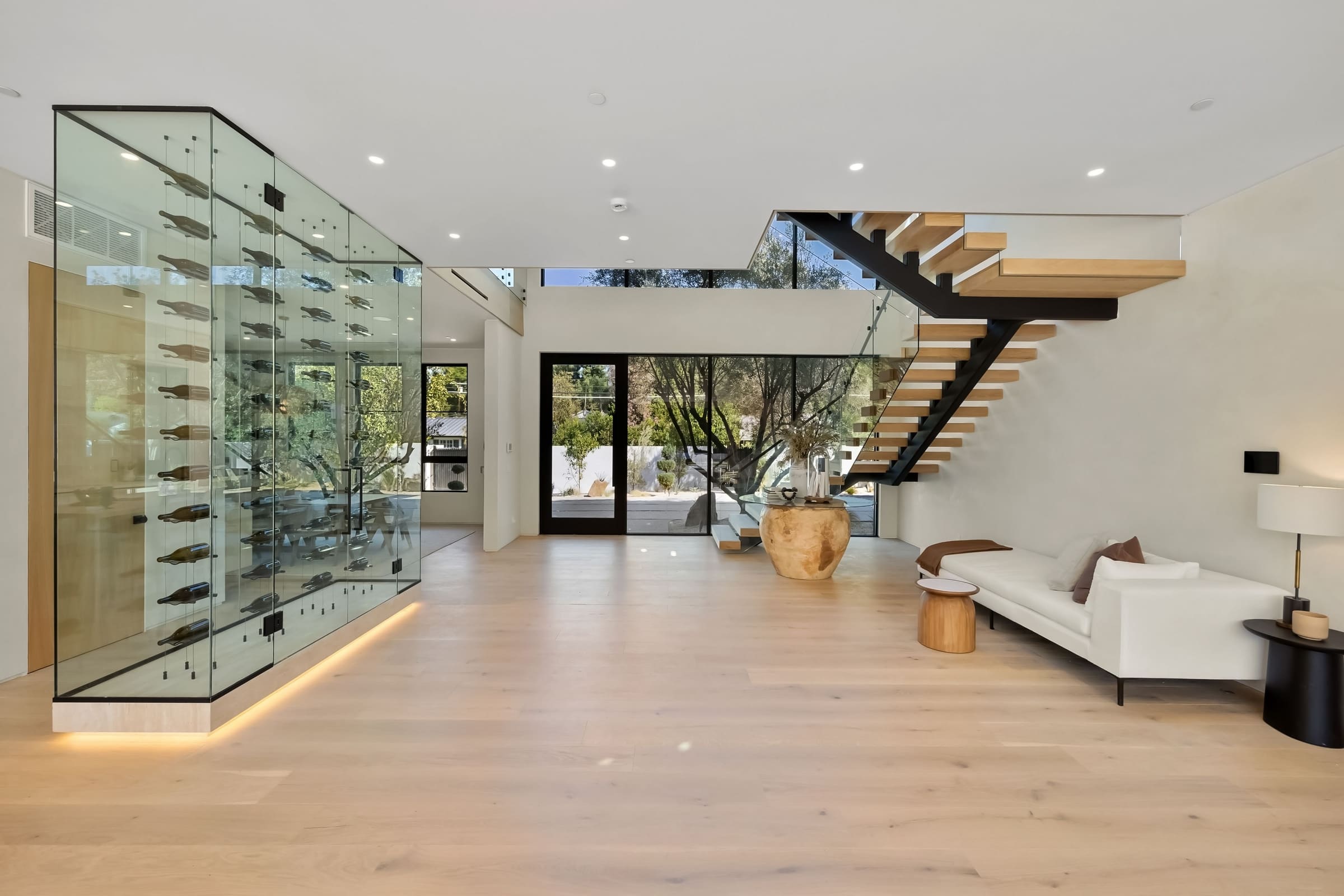 Custom glass-enclosed wine room beside a floating staircase
